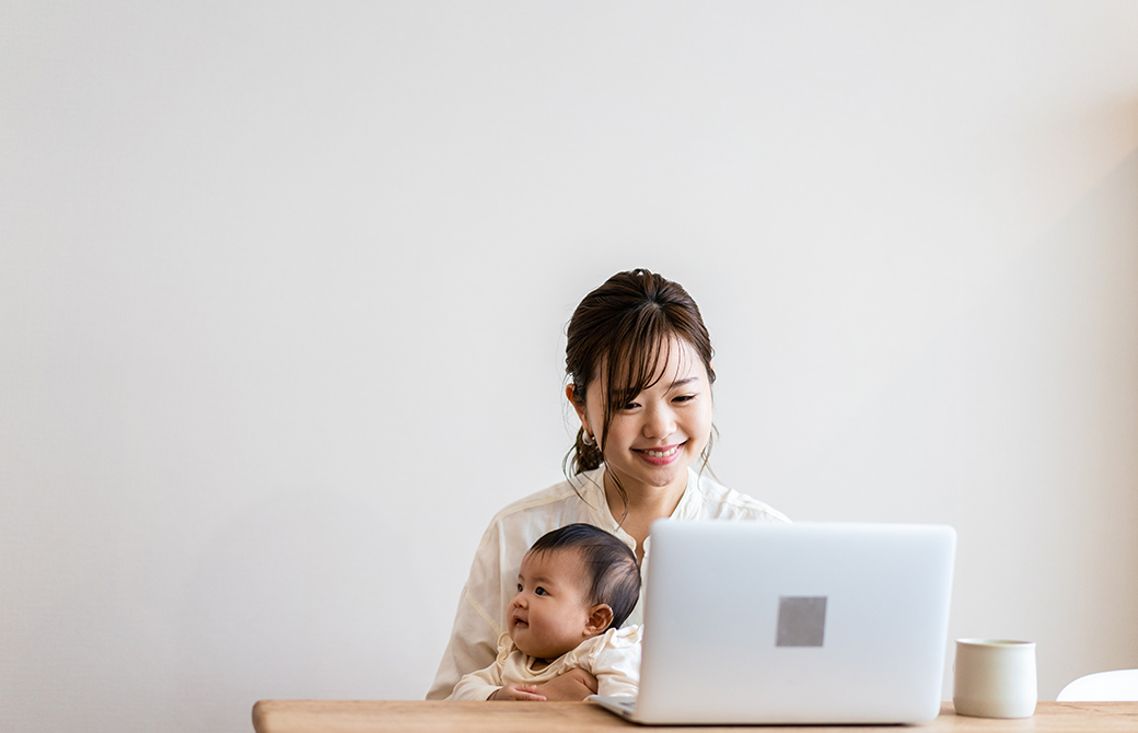 赤ちゃんと一緒にパソコンを見ている母親