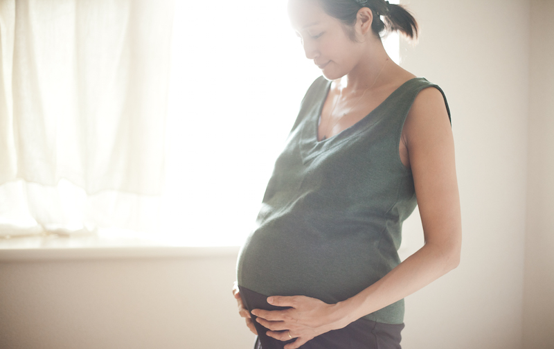 光がさす室内でサントーシマ香先生が妊娠したお腹を包み込むように手を置いている