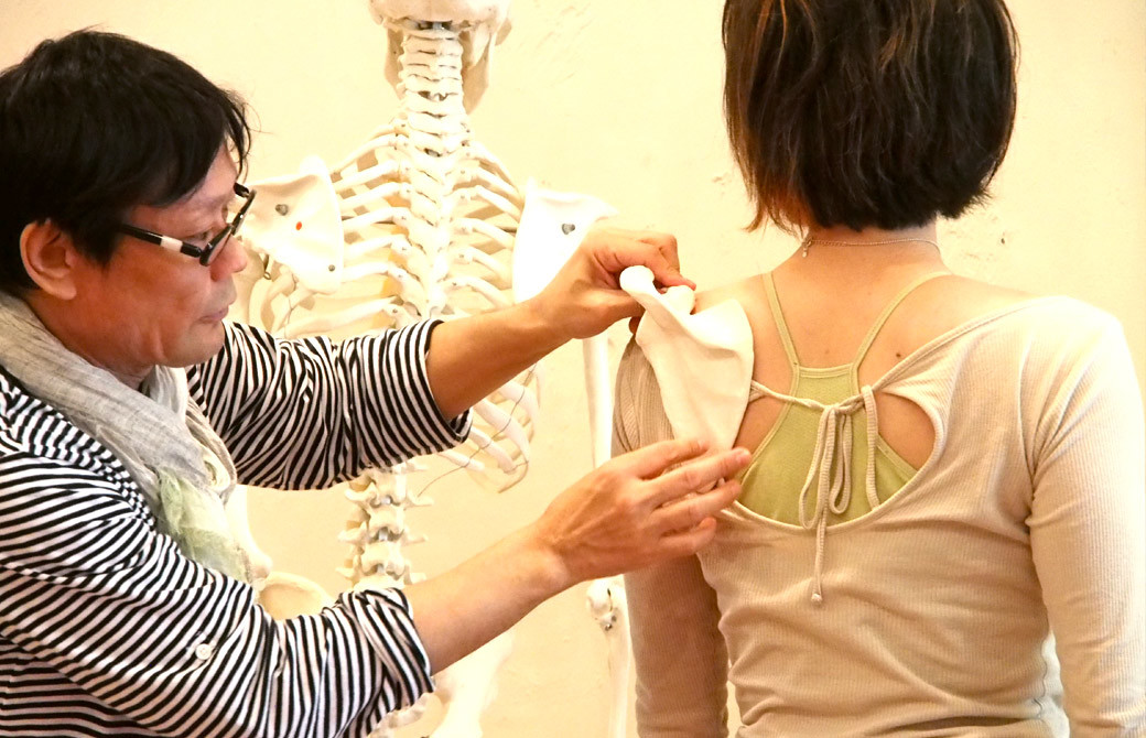 ヨガ講師（内田かつのり）が生徒さんの肩甲骨に模型を体に当てて形を確認している様子