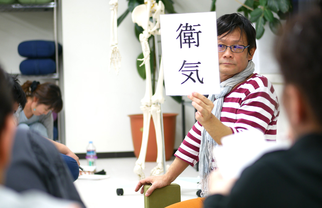 経絡ワークショップの講座風景。講師(内田かつのり)が衛気(えき)の資料を生徒に見せている様子
