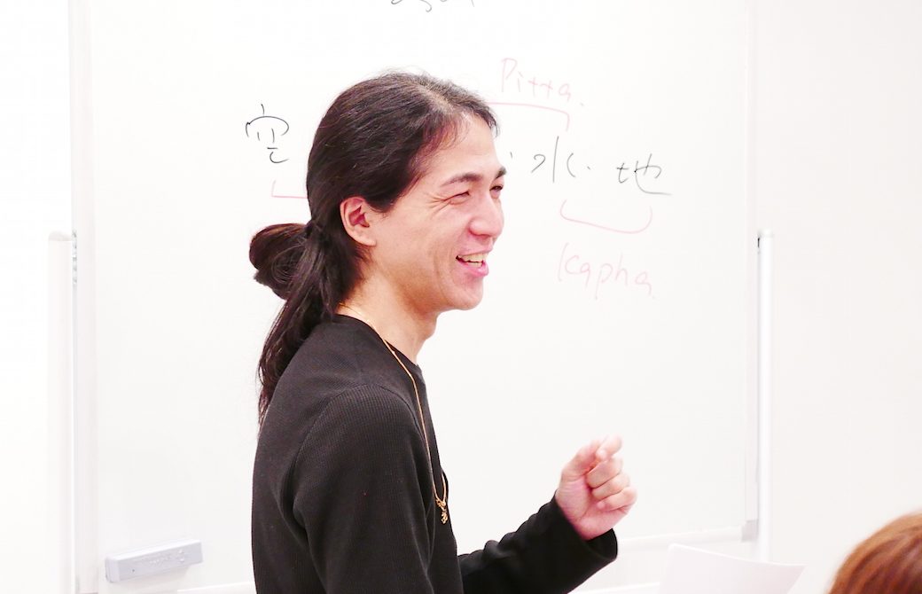 ホワイトボードの前で笑顔で講義している和也先生
