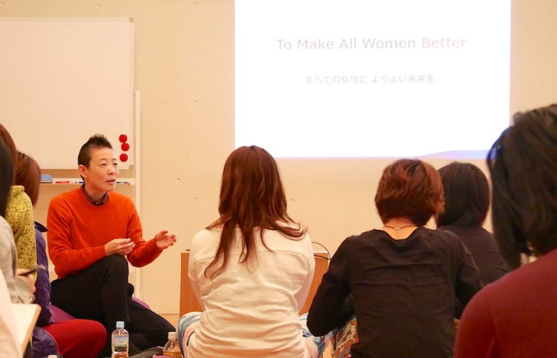 全ての女性によりよい未来をと映し出されているスライドの前で話をしている高尾先生