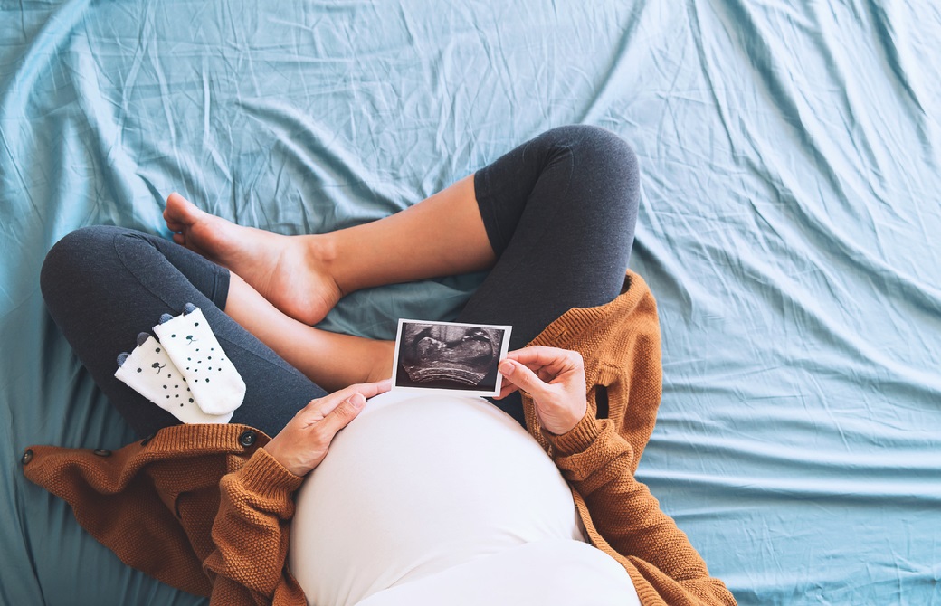 妊婦さんがあぐらをかいて座りながら赤ちゃんのエコー写真を見ている